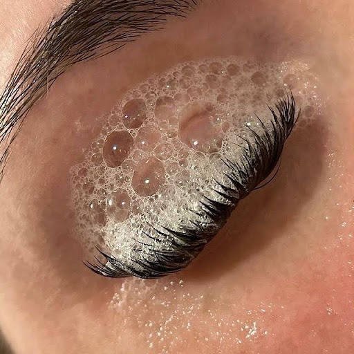 Closed eye with long lashes and cleansing bubbles on the eyelid.