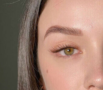 Close-up of a well-groomed eyebrow and eye with long lashes on a woman with light skin and brown hair.